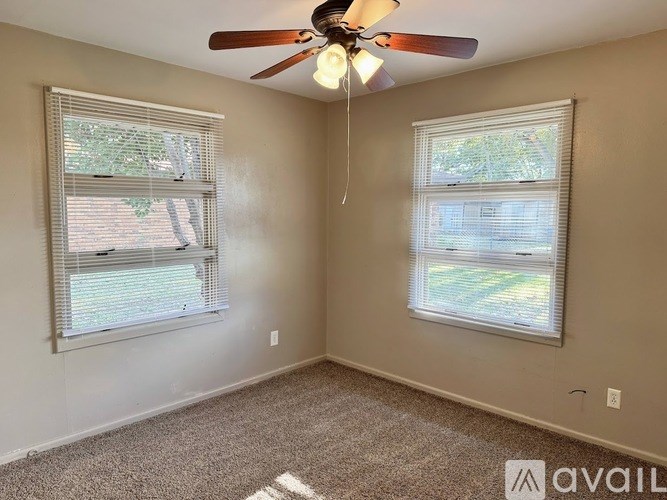 A room with a ceiling fan and two windows.