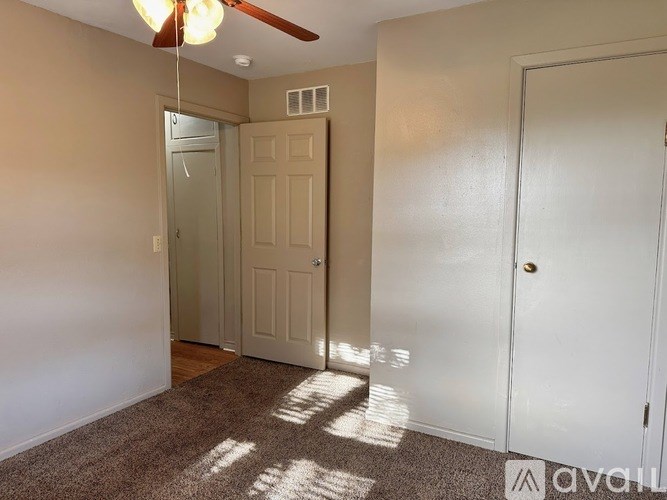 A room with a carpeted floor, a ceiling fan, and two doors.