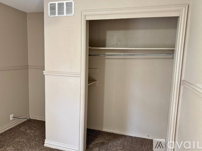 A white closet with a shelf and a vent on the wall.