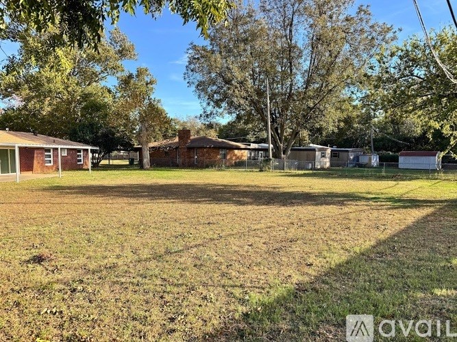 A grassy field with trees and houses in the background.