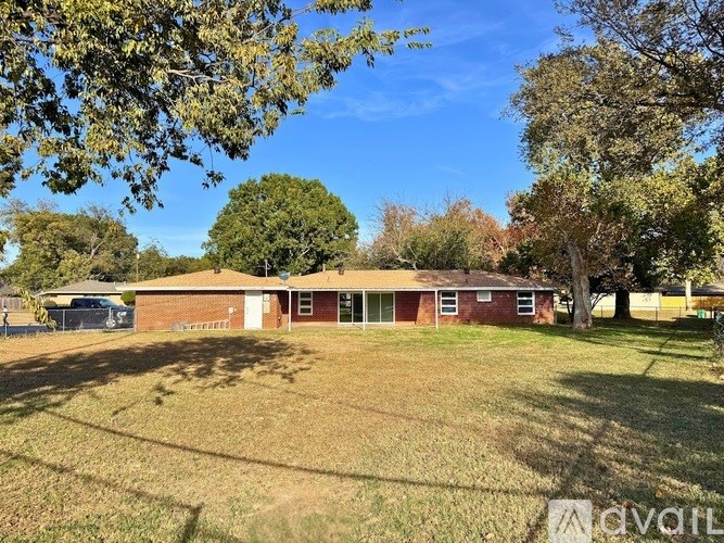 A red brick building with a white door and windows is surrounded by a grassy field.