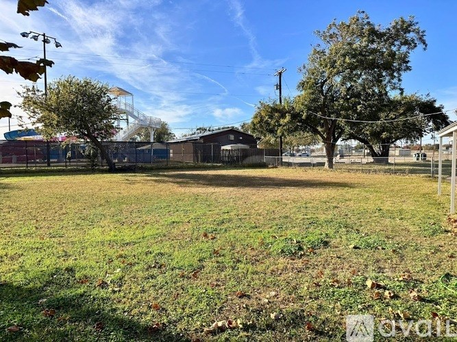A grassy field with trees and a fence in the background.