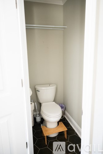 A white toilet in a small bathroom with a wooden stool.