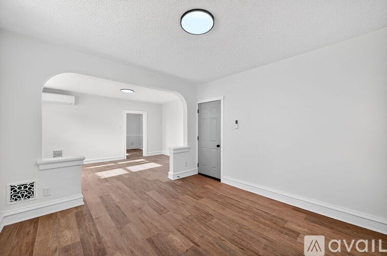 A spacious room with wooden flooring and white walls.
