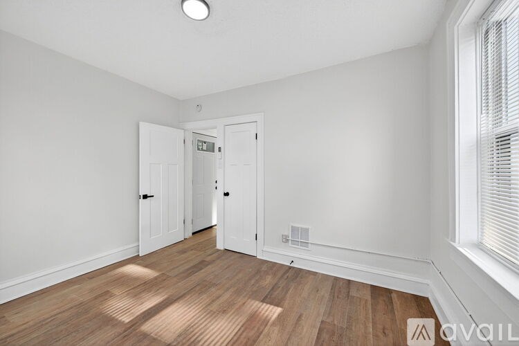A room with white walls and wooden flooring, with a window on the right side.