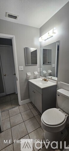 A bathroom with a toilet, sink, mirror, and lighting fixtures.