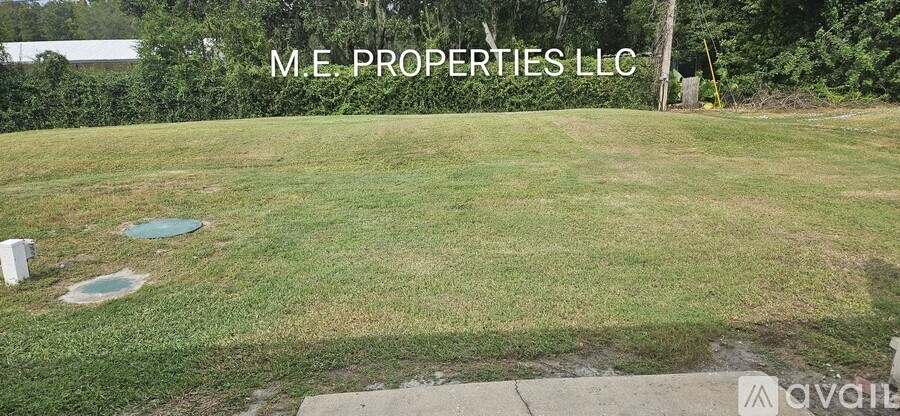 A grassy area with a sign that says "M.E. PROPERTIES LLC" and a logo in the bottom right corner.