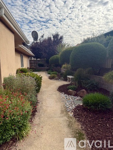 A garden pathway with a house and trees in the background.