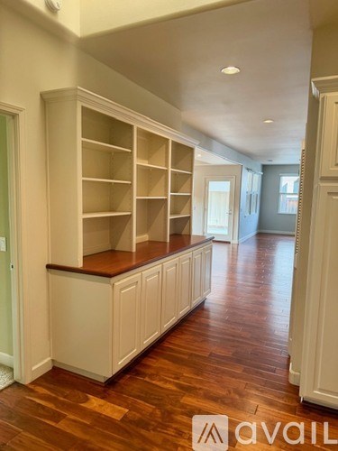 A long hallway with a wall of shelves and a wood floor.
