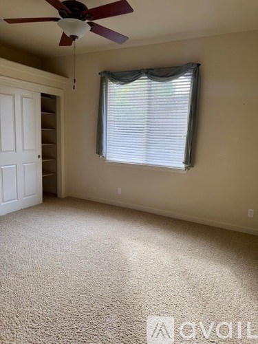 A room with a carpeted floor, a ceiling fan, and a window with blinds.