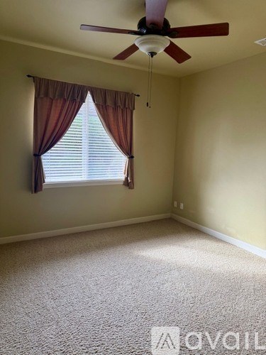 A room with a ceiling fan and a window with curtains.