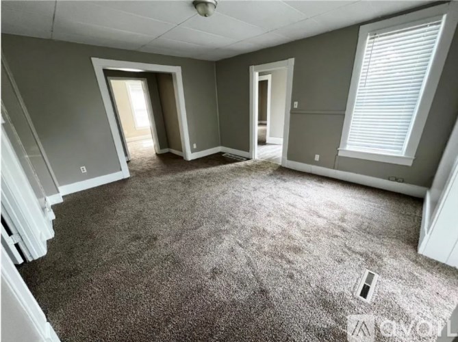 A spacious room with carpeted floor and a staircase on the left side.