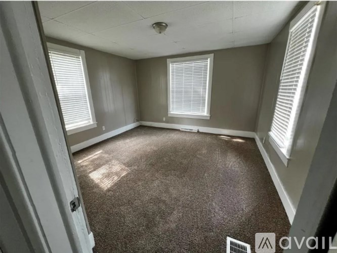 A room with carpeted floor and a window with blinds.