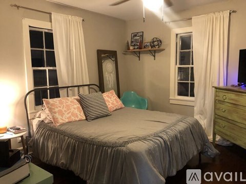 A bedroom with a bed, a dresser, and a window with curtains.