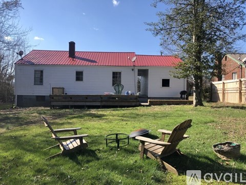 A white house with a red roof is surrounded by a grassy yard with two chairs and a table.
