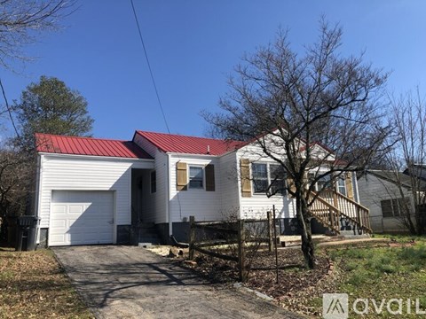 A white house with a red roof is surrounded by a fence and a bare tree.