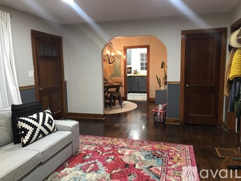A living room with a grey couch and a rug with a black and white pillow on it.