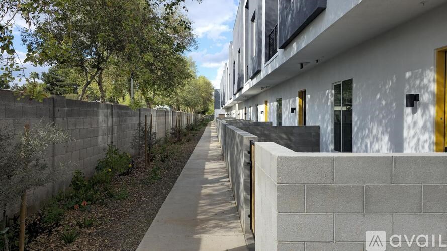 A long white building with yellow doors and windows is surrounded by a concrete wall and trees.