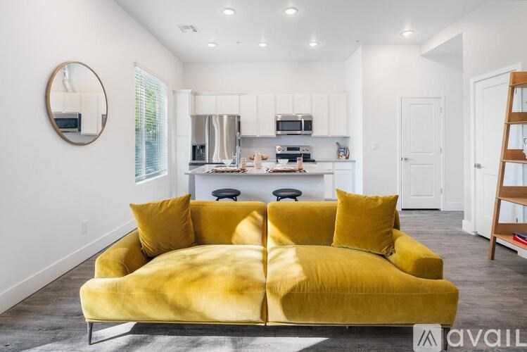 A yellow couch is in the middle of a white room with a kitchen in the background.