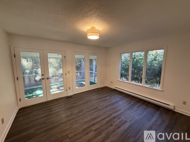 A room with a wooden floor and a large window with a view of trees.