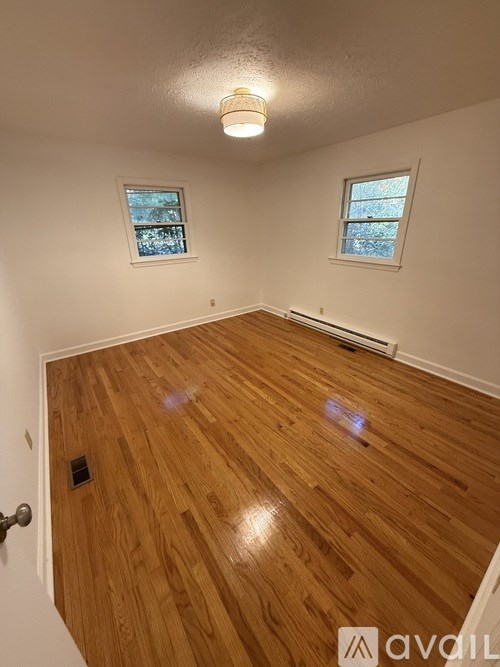A room with wooden flooring and two windows.
