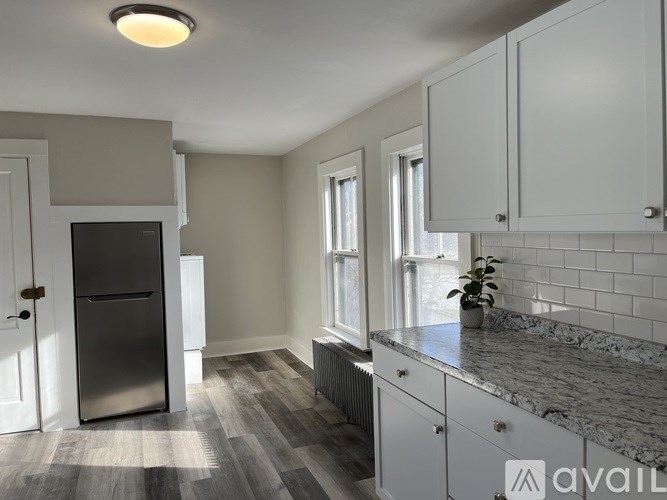 A kitchen with a black fridge, white cabinets, and a marble countertop.