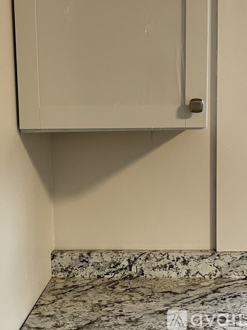 A white cabinet with a silver handle is mounted on a wall above a marble floor.