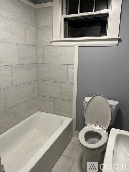 A white toilet sits next to a bathtub in a bathroom with grey walls.