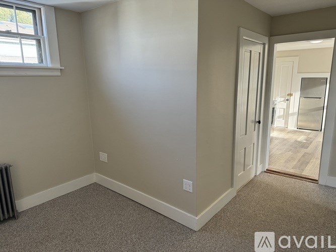 A room with a carpeted floor, a window, and a door leading to another room.