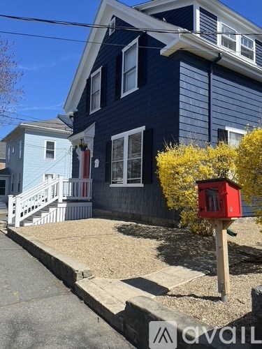 A red mailbox is on a wooden post in front of a blue house.