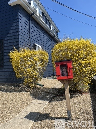 A red mailbox is on a wooden post in front of a blue house.