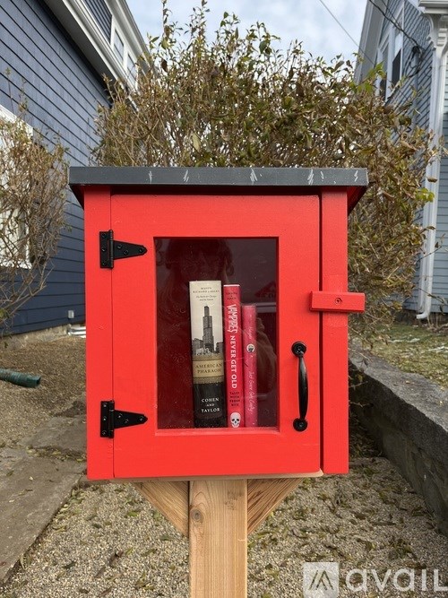 A red birdhouse with a black roof and a black latch is on a wooden post.