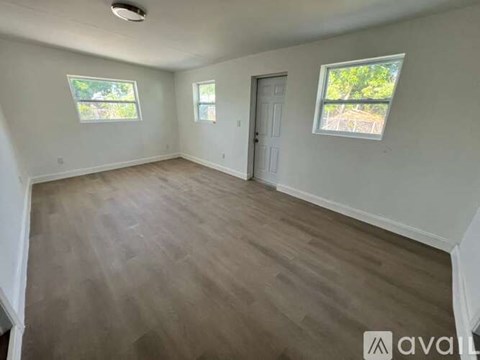 A room with wooden flooring and white walls, with a door and two windows.