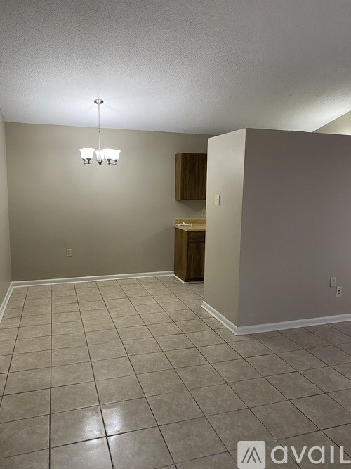 A room with beige walls and tiled flooring with a chandelier hanging from the ceiling.