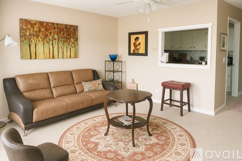A living room with a brown leather sofa, a round wooden table, and a rug.