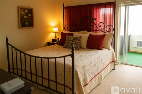 A bed with a red and white comforter and pillows in a room with a window.