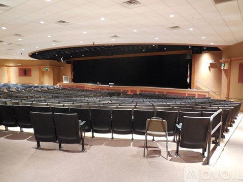 A large auditorium with rows of black chairs facing a stage.