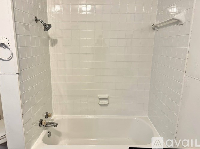 A white tiled bathroom with a white tub and shower.
