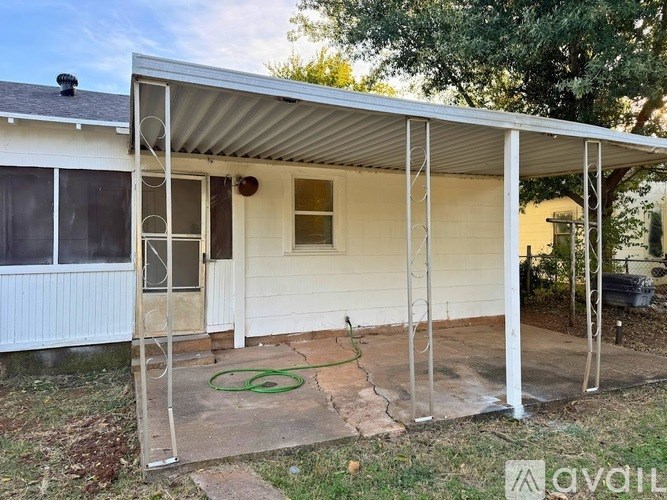 A white house with a covered patio and a green hose.