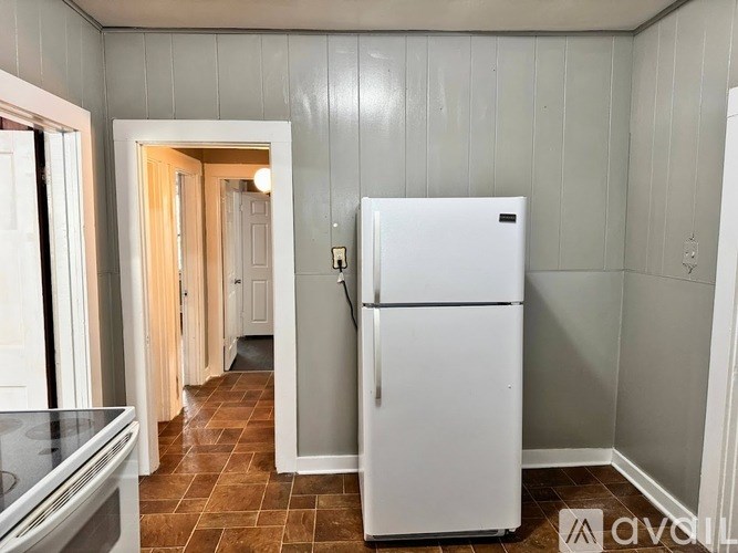 A white refrigerator in a kitchen with grey walls and brown tiles.
