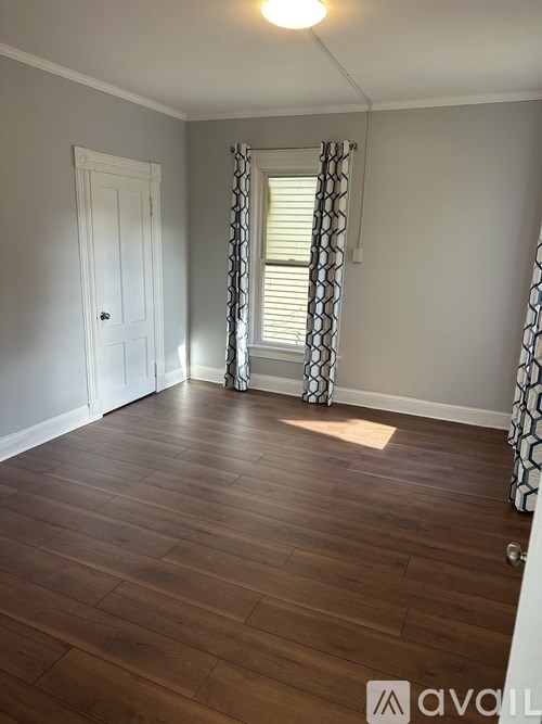 A room with wooden flooring and a window with curtains.