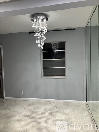 A chandelier hangs from the ceiling in a room with a grey wall and a window.