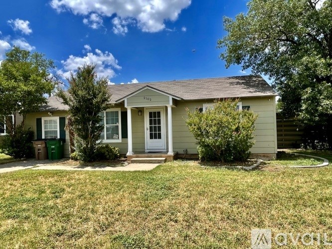 A house with a green trash bin in front of it.
