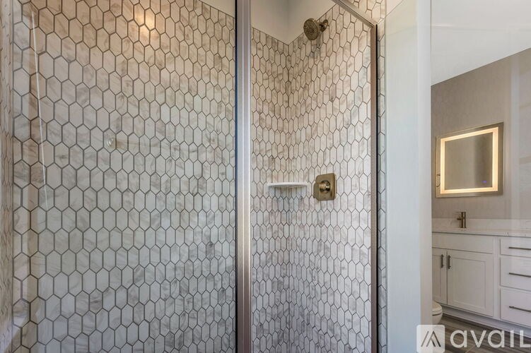 A shower with a glass door and a hexagonal tile wall.