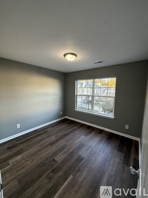 A room with wooden flooring and a window showing a view of buildings outside.