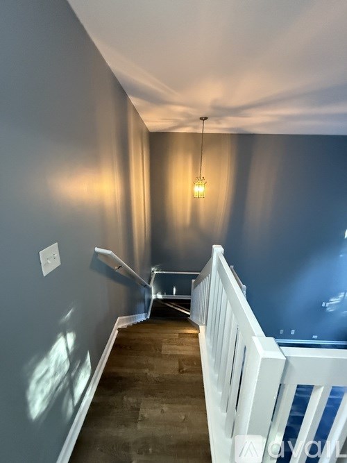 A long hallway with a white railing on the right and a light hanging from the ceiling.