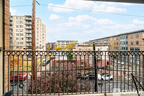 A view from a balcony looking down a street lined with cars and buildings.