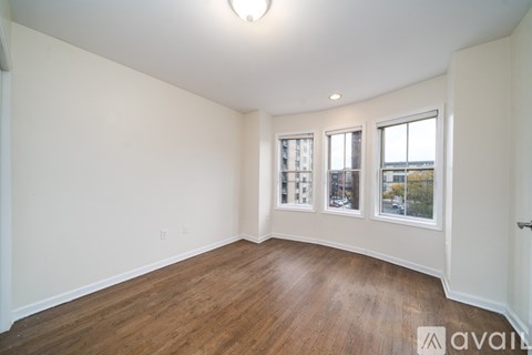 A room with wooden floors and white walls, with a window showing a city view.