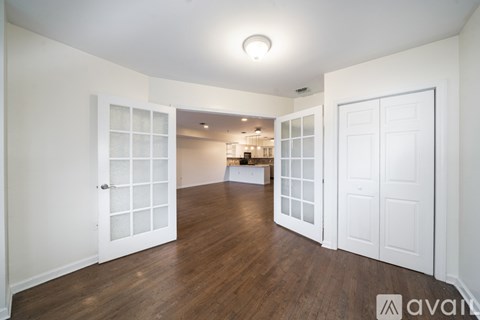 A room with white walls and wooden floors, with a doorway leading to another room.