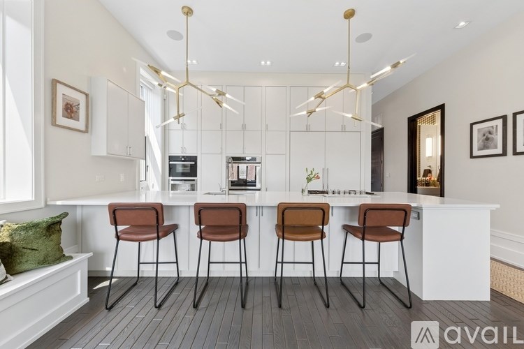 A modern kitchen with white cabinets and a white island with three brown chairs.